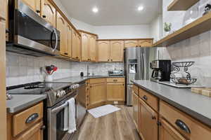 Kitchen featuring wood cabinetry, stainless steel appliances, grey countertops, white tiled backsplash, and wood-finish flooring