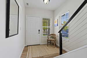 Entryway featuring wood-finish flooring, a white paneled door, and dual windows with blinds