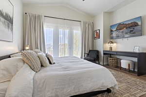 Vaulted ceiling bedroom featuring French doors opening to a balcony with black iron railings, wood-finish flooring, and built-in wall sconces