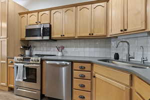 Kitchen featuring stainless steel appliances, wood-finish cabinetry, a curved sink, a gooseneck faucet, and a textured tile backsplash