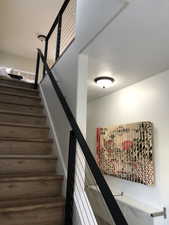 Modern staircase featuring wood-finish treads, black metal handrails, and cable railing