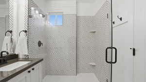 Contemporary bathroom featuring a walk-in shower with geometric patterned tile and a frameless glass enclosure, a window, hexagonal mosaic floor tile, a single vanity with a rectangular sink, and dark-finish hardware