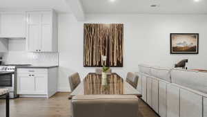 Open-concept living space with wood-finish flooring, white cabinetry, dark countertops, and a full tile backsplash