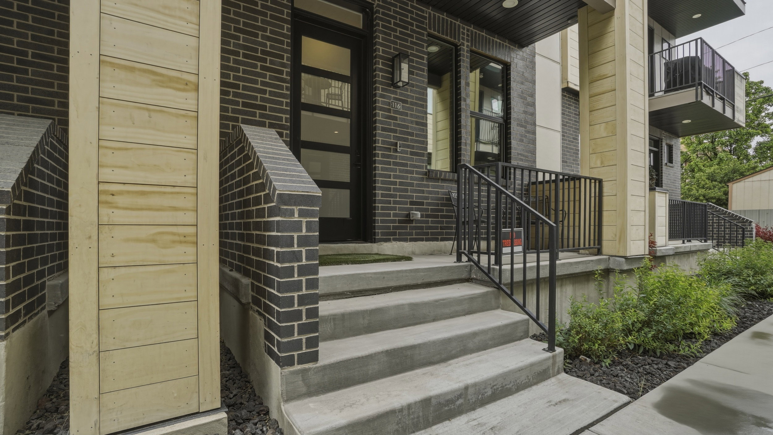 Modern multi-level exterior with dark brickwork, light wood-finish siding, and a black-framed entry door with frosted glass panels