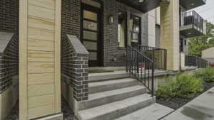Modern multi-level exterior with dark brickwork, light wood-finish siding, and a black-framed entry door with frosted glass panels
