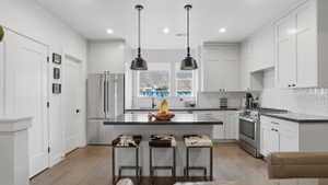 Modern kitchen featuring white shaker cabinetry, stainless steel appliances, dark countertops, and a central island with pendant lighting