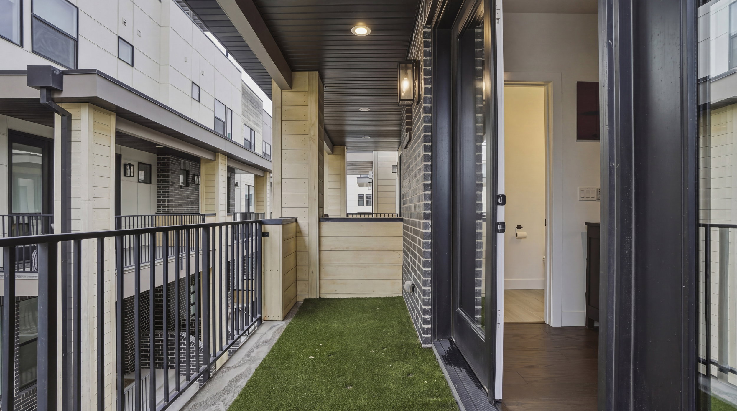 Outdoor balcony featuring artificial turf flooring, black metal railings, and a black brick exterior wall