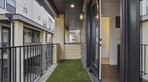 Outdoor balcony featuring artificial turf flooring, black metal railings, and a black brick exterior wall