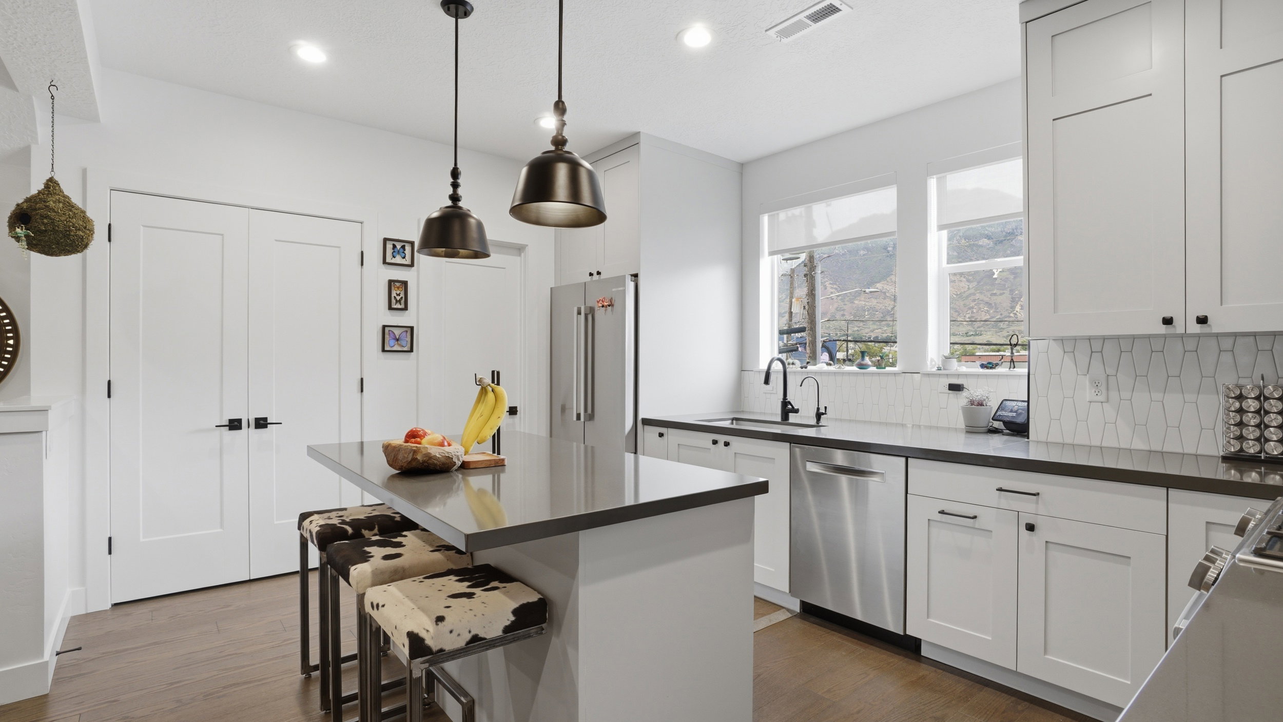 Modern kitchen featuring white shaker cabinetry, dark countertops, stainless steel appliances, and a central island with pendant lighting