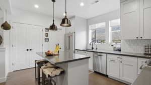 Modern kitchen featuring white shaker cabinetry, dark countertops, stainless steel appliances, and a central island with pendant lighting