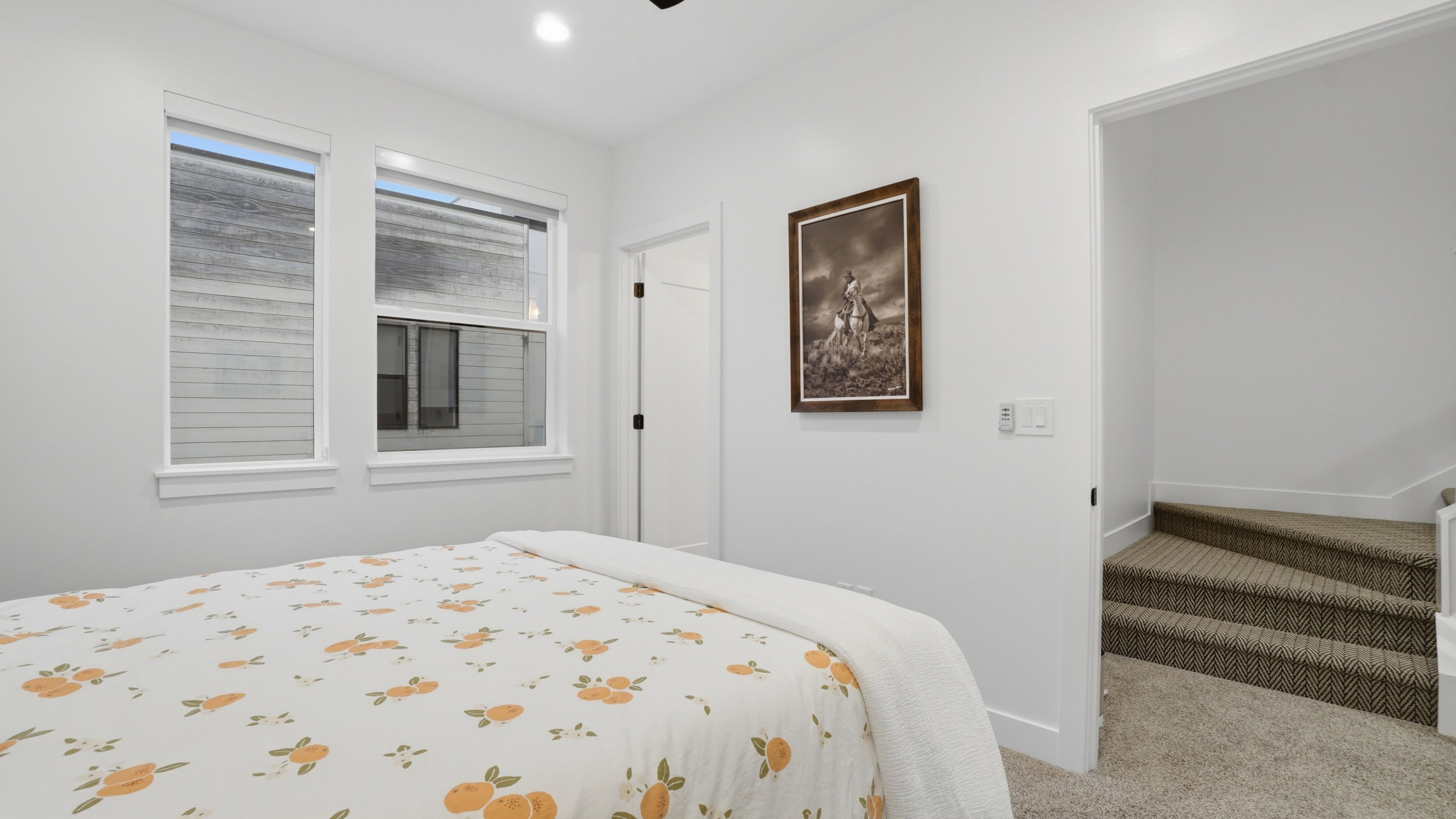 Bright interior space featuring two windows with white trim, recessed lighting, a paneled door with black hardware, white walls, and textured carpeted stairs