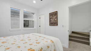 Bright interior space featuring two windows with white trim, recessed lighting, a paneled door with black hardware, white walls, and textured carpeted stairs