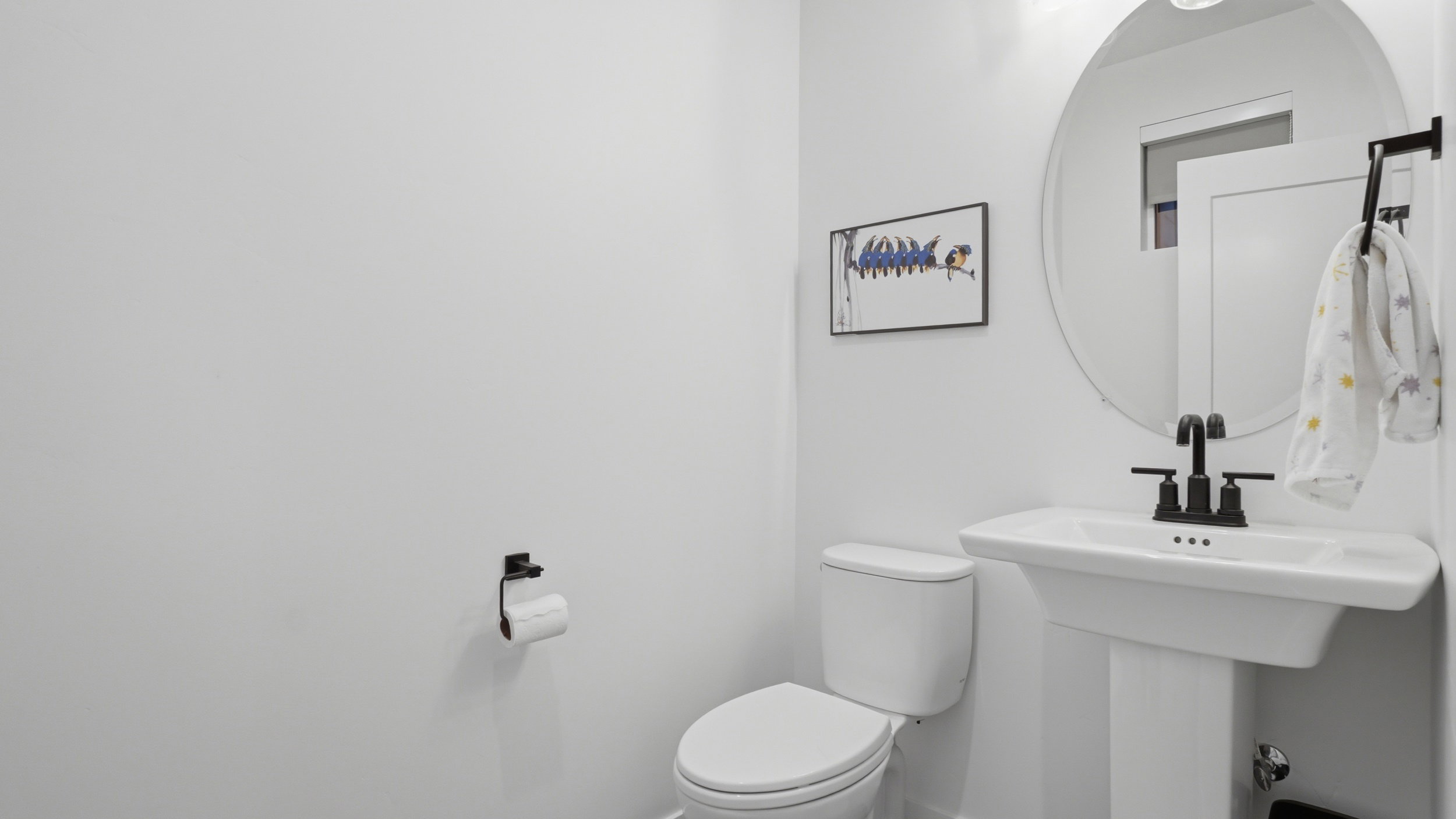 Pedestal sink with matte black faucet, wall-mounted circular mirror, and recessed lighting