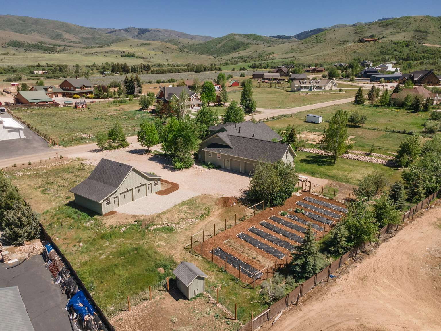 Spacious property featuring a main residence with an attached multi-car garage, a detached multi-car garage, and an expansive garden area with structured raised beds