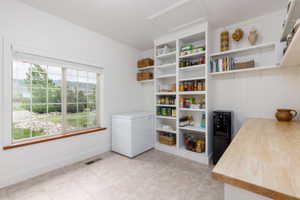 Spacious pantry featuring extensive built-in shelving, a large window with natural light, tiled flooring, and a wood-finish countertop