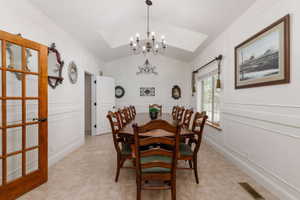 Vaulted ceiling featuring a chandelier, panel molding, wood-finish flooring, a French pane door, and a window with wood trim
