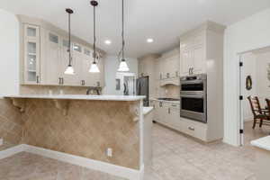Kitchen featuring light-toned cabinetry, stainless steel double wall ovens, a coordinating refrigerator, and a gas cooktop