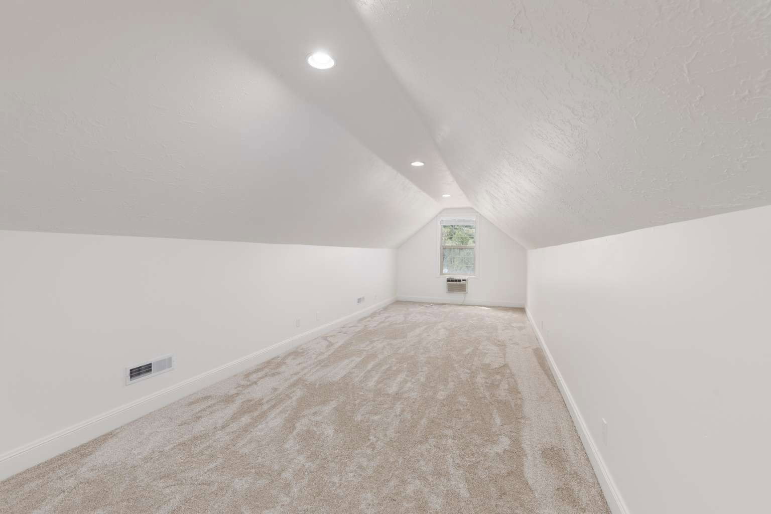 Spacious room featuring vaulted ceilings, light neutral carpeting, recessed lighting, white baseboards, and a window with a window-mounted unit