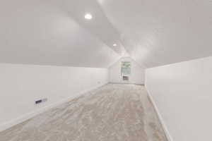 Spacious room featuring vaulted ceilings, light neutral carpeting, recessed lighting, white baseboards, and a window with a window-mounted unit