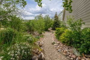 Gravel pathway bordered by river rocks, leading through dense foliage and flowering plants