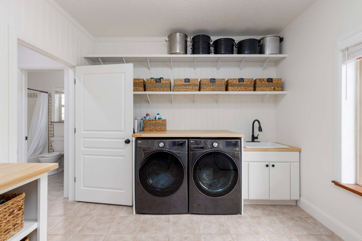 Dedicated laundry area featuring a built-in sink with a matte black faucet, light wood-finish countertops, and white base cabinetry