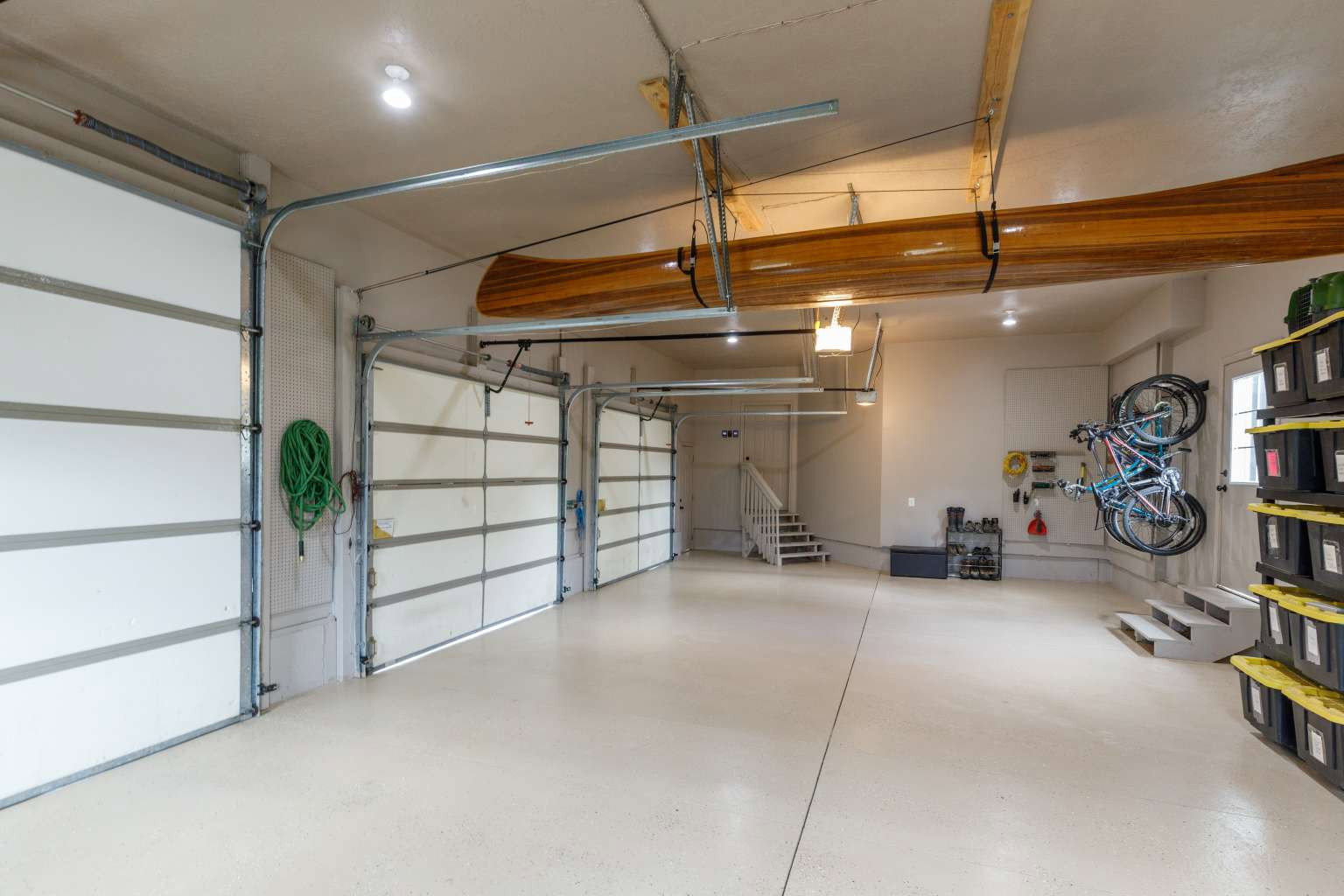 Spacious multi-bay garage with overhead lighting, light-toned flooring, exposed structural beams, and a white door providing exterior access