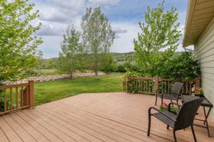 Spacious outdoor deck with composite decking and wood railings, overlooking a manicured lawn, mature trees, and natural rock features