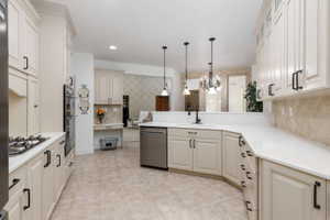 Kitchen featuring light-toned cabinetry with dark hardware, a gas cooktop, built-in double ovens, and a tile backsplash