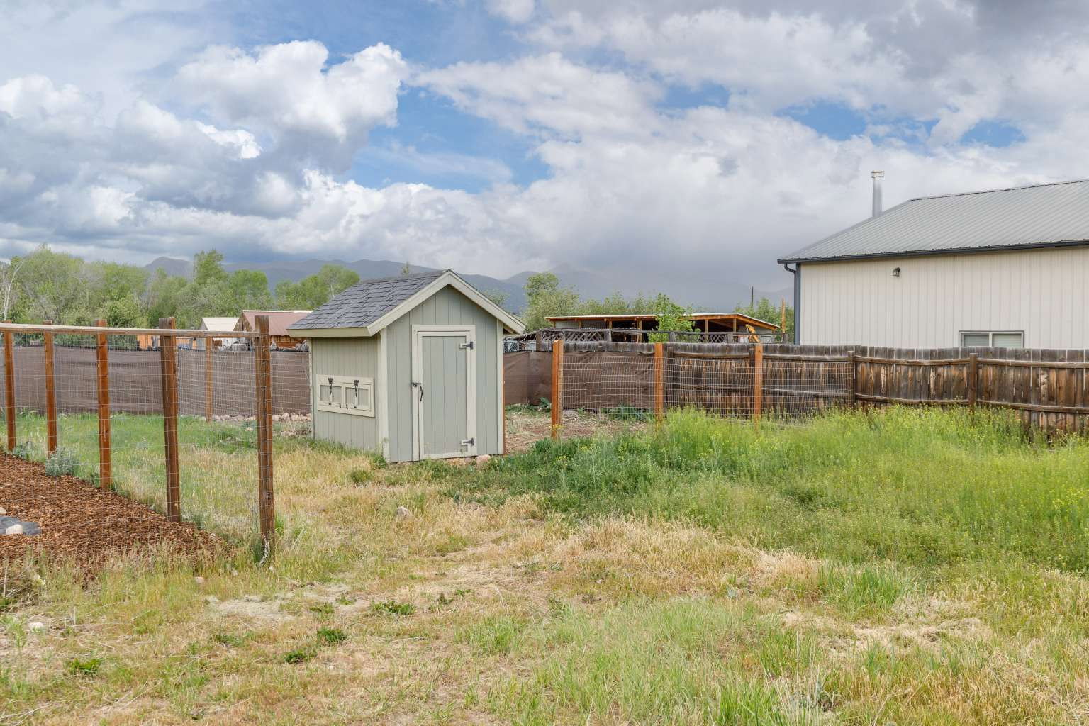 Rear yard featuring a light green storage shed with a dark shingle roof, wood fencing, and a wire mesh fence