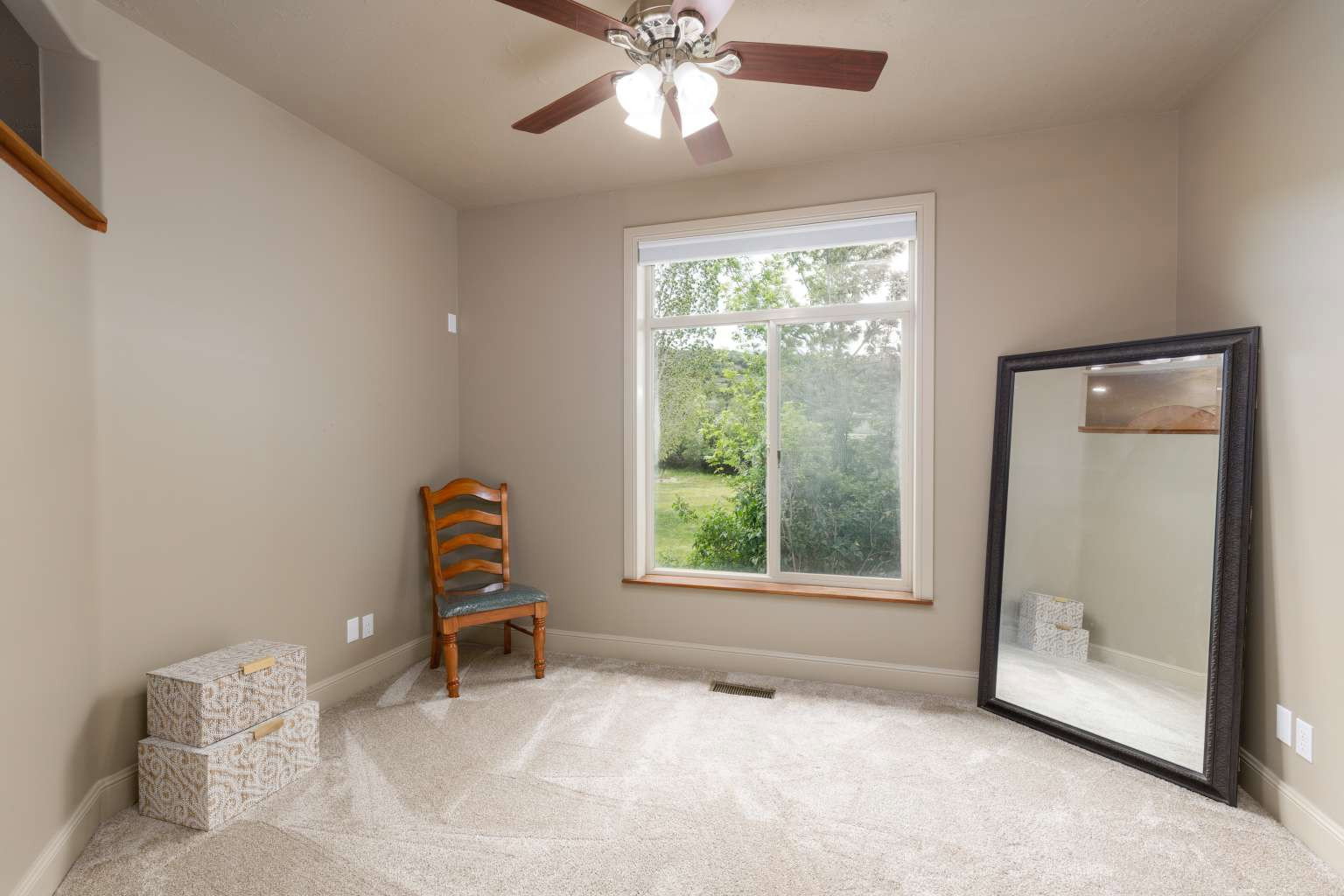 Carpeted room featuring a large window, a ceiling fan with light fixture, and neutral painted walls