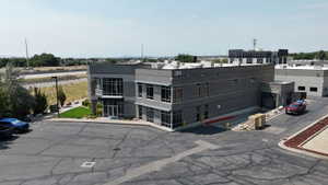 Contemporary commercial building featuring a two-story glass facade, dark gray brick exterior, a loading dock, and an expansive asphalt parking area