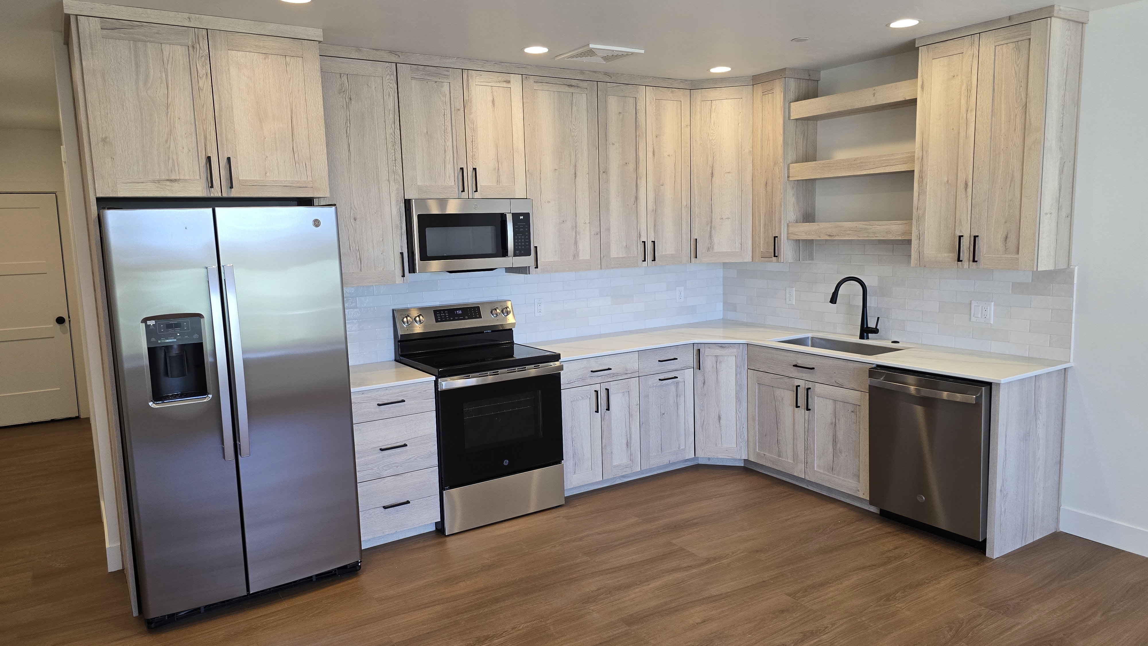 Kitchen featuring wood-finish flooring, light-toned cabinetry with matte black hardware, stainless steel appliances, white subway tile backsplash, and recessed lighting