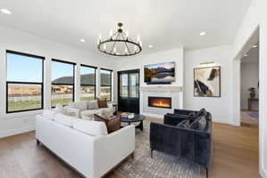 Spacious living area featuring expansive windows, wood-finish flooring, a contemporary fireplace with a stone surround, recessed lighting, and an ornate chandelier