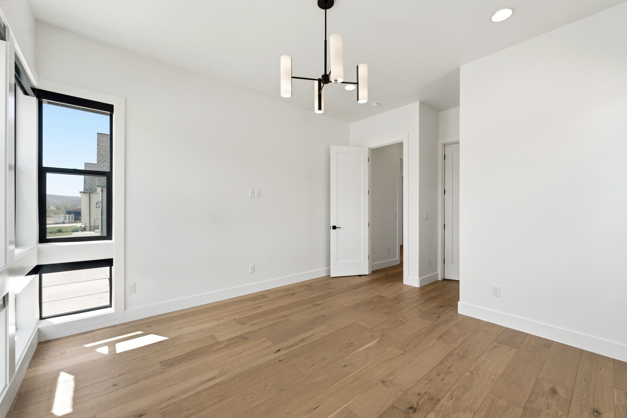 Room featuring wood-finish flooring, white walls, and a contemporary chandelier