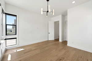 Room featuring wood-finish flooring, white walls, and a contemporary chandelier
