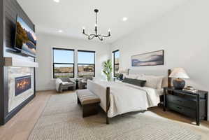 Bedroom featuring a built-in fireplace with a tiled surround, wood-finish flooring, a contemporary chandelier, recessed lighting, and multiple windows