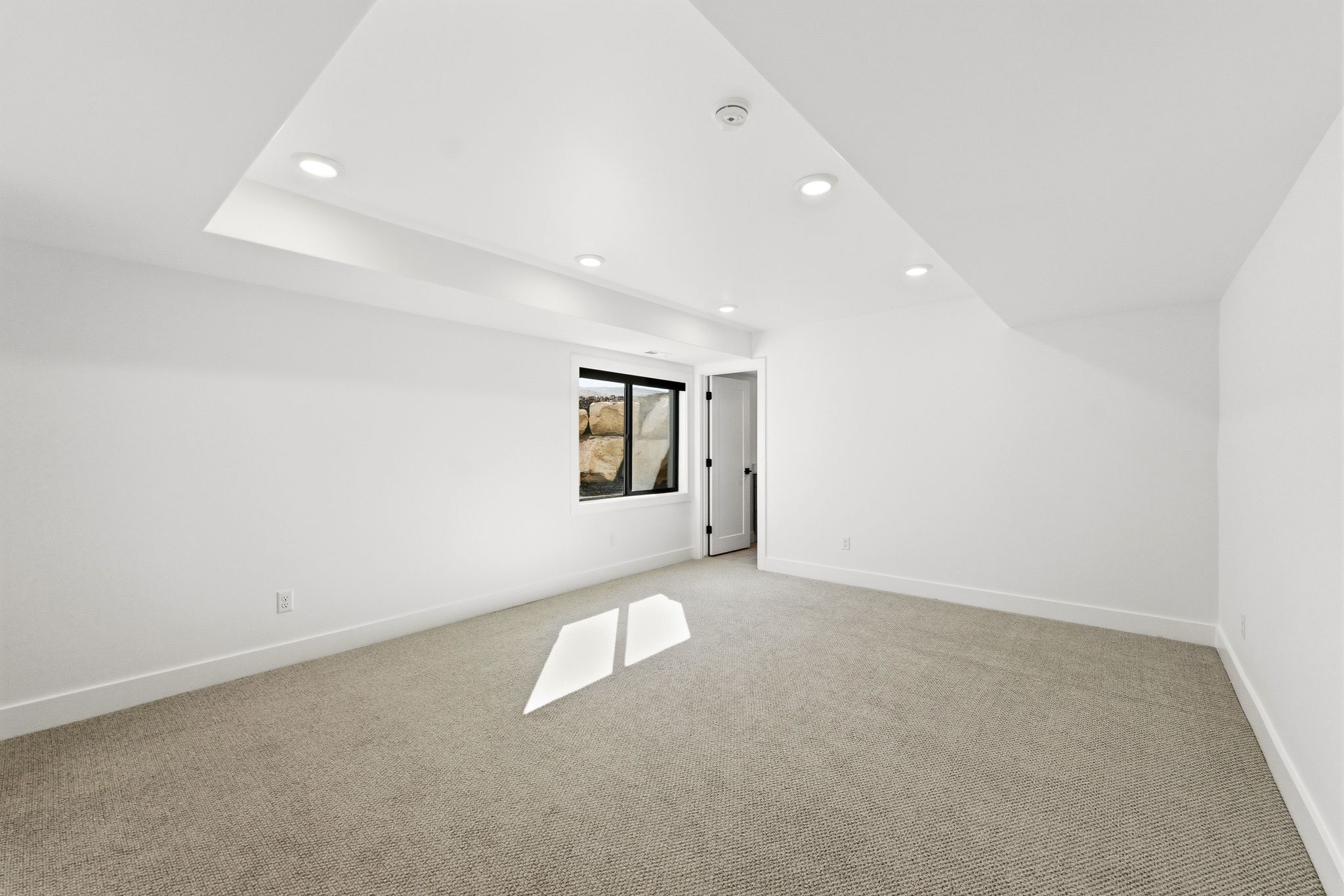 Carpeted room featuring recessed lighting, a white painted door, a window with black trim, and a tray ceiling