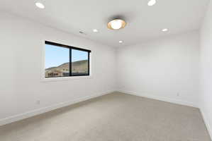 Light-filled room featuring a broad window with black framing, recessed ceiling lighting, a central flush-mount fixture, high baseboards, and light-toned carpeting