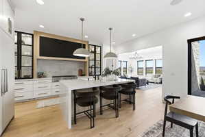 Gourmet kitchen featuring a waterfall island, light wood-finish flooring, white cabinetry, a large range with a stone backsplash, and recessed lighting