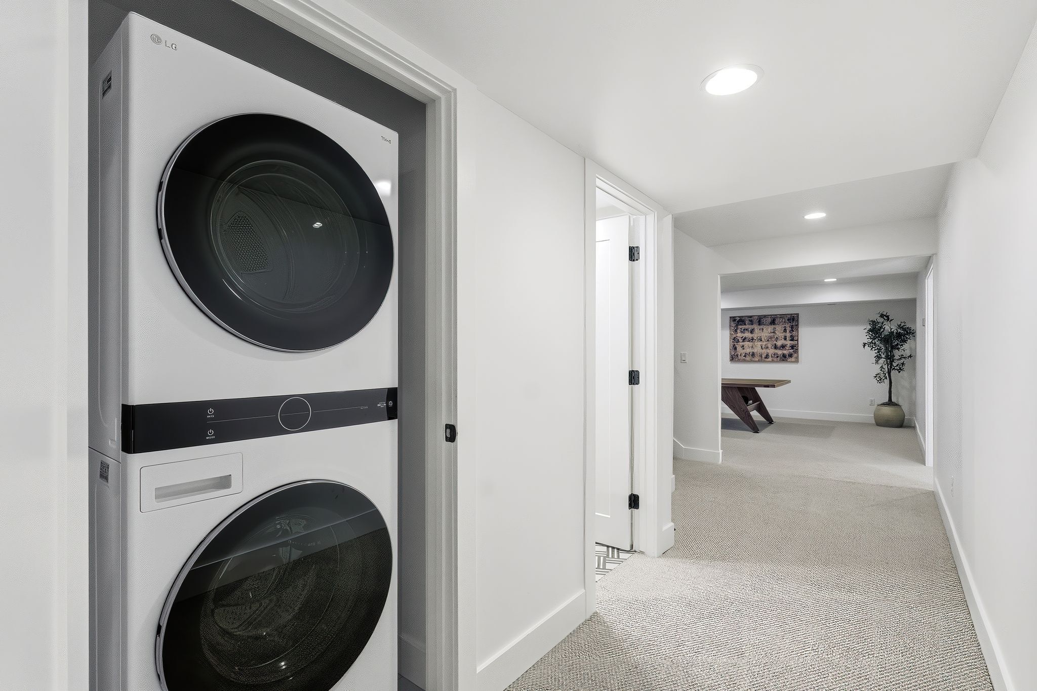 Integrated laundry closet featuring a stackable washer and dryer, recessed lighting, white walls, and light-toned carpet flooring throughout the hallway