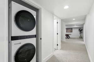 Integrated laundry closet featuring a stackable washer and dryer, recessed lighting, white walls, and light-toned carpet flooring throughout the hallway