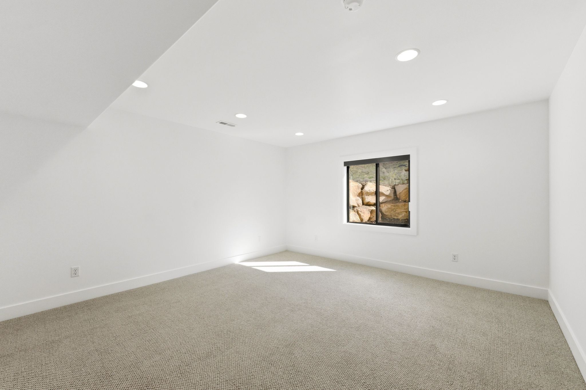 Spacious room with recessed lighting, light-toned carpeting, white walls, and a window featuring a natural rock backdrop