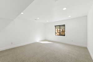 Spacious room with recessed lighting, light-toned carpeting, white walls, and a window featuring a natural rock backdrop