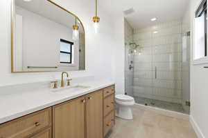Bathroom featuring a light wood-finish vanity with a white countertop and undermount sink, brass-finish fixtures, an arched mirror, and pendant lighting