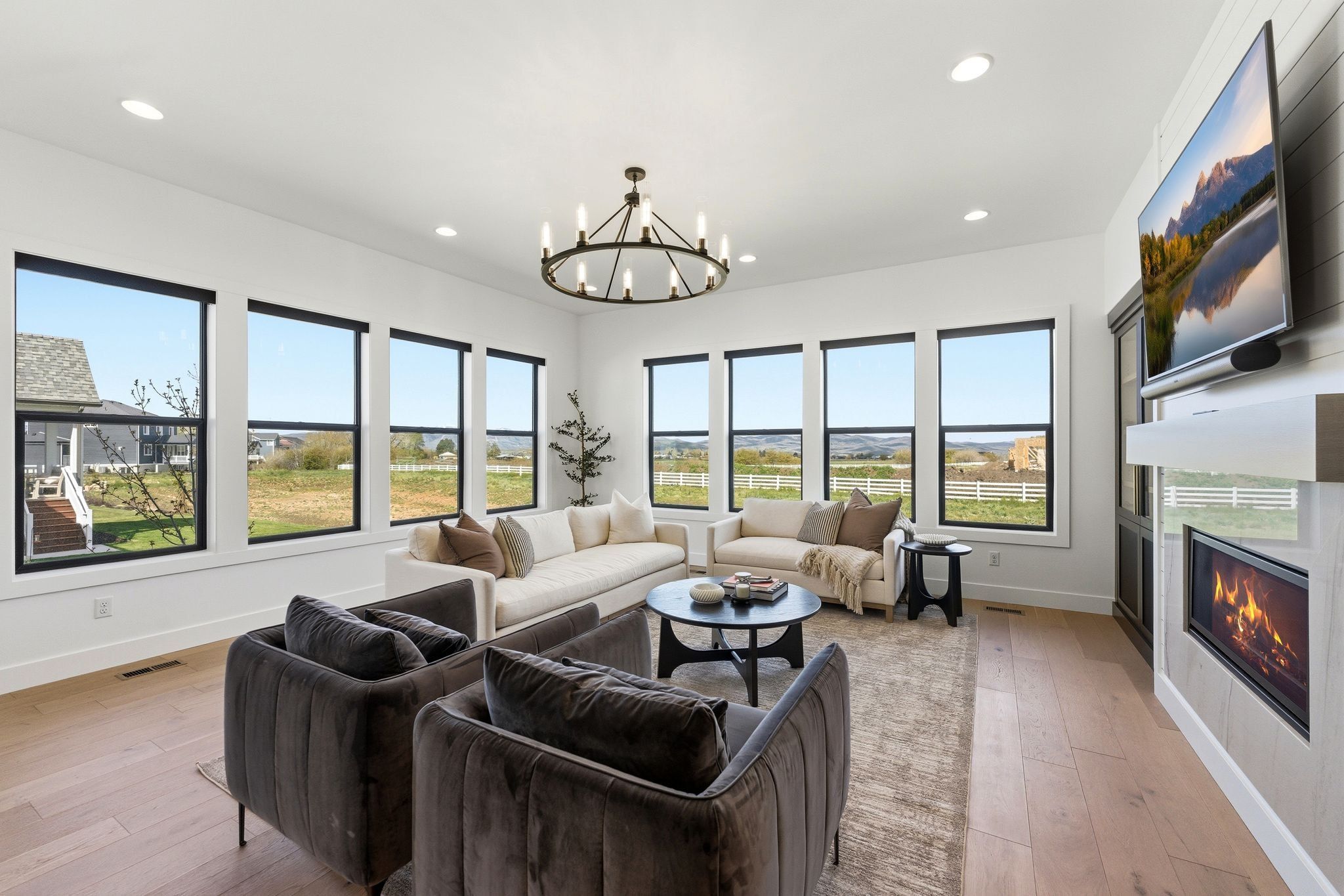Expansive living area featuring multiple large windows, wood-finish flooring, a wall-mounted fireplace, a built-in entertainment center, and a contemporary chandelier