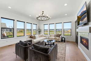 Expansive living area featuring multiple large windows, wood-finish flooring, a wall-mounted fireplace, a built-in entertainment center, and a contemporary chandelier