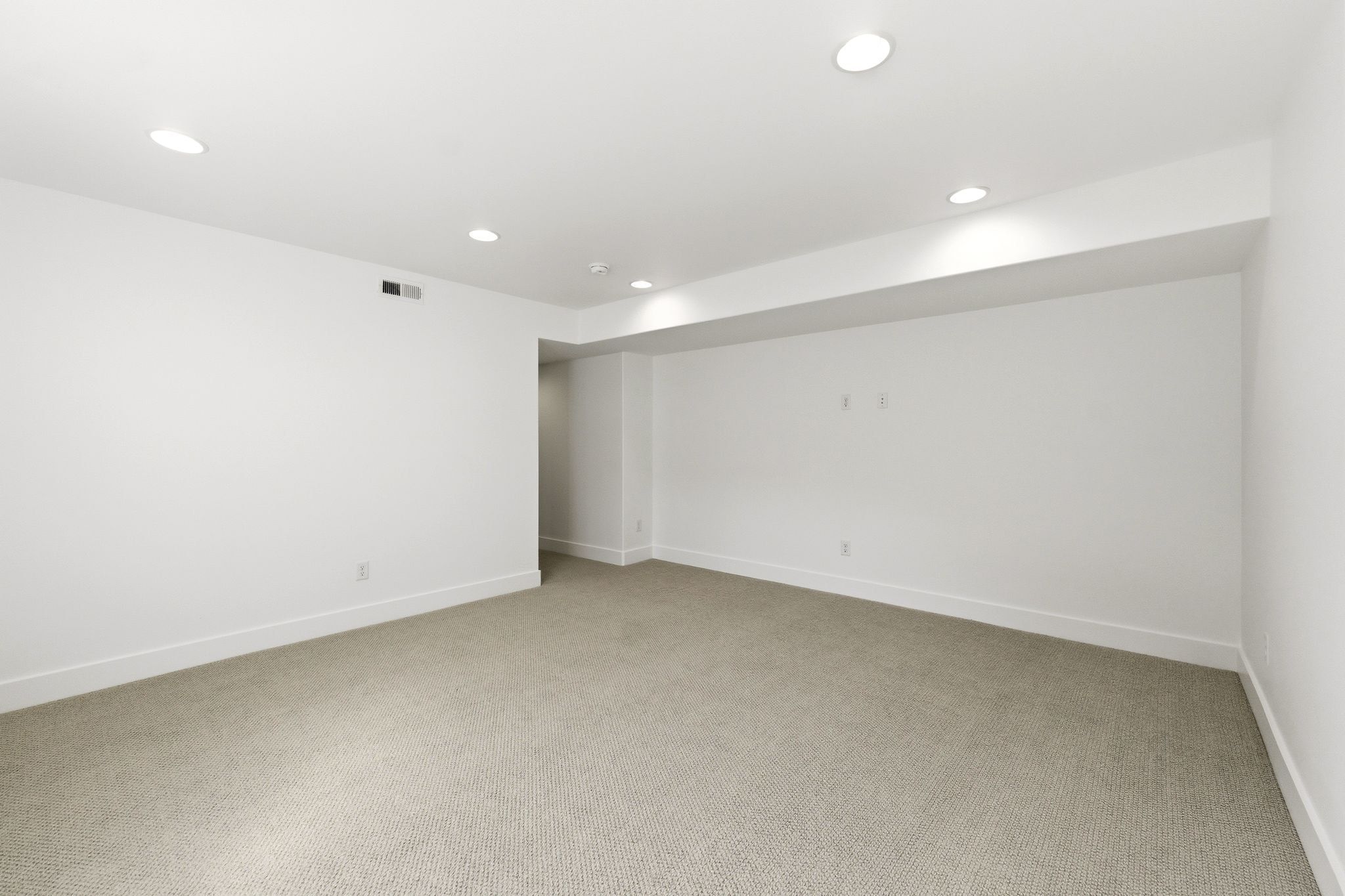 Spacious room featuring neutral carpeting, white walls, recessed lighting, white baseboards, and HVAC vents