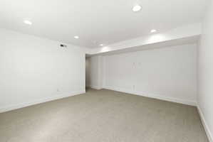 Spacious room featuring neutral carpeting, white walls, recessed lighting, white baseboards, and HVAC vents