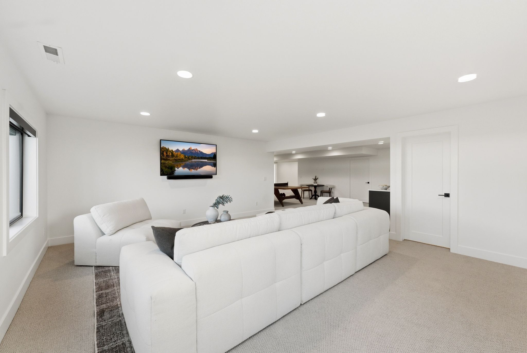 Spacious recreation room featuring recessed lighting, a mounted media display, neutral carpeting, and a white paneled interior door with matte black hardware