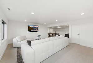 Spacious recreation room featuring recessed lighting, a mounted media display, neutral carpeting, and a white paneled interior door with matte black hardware